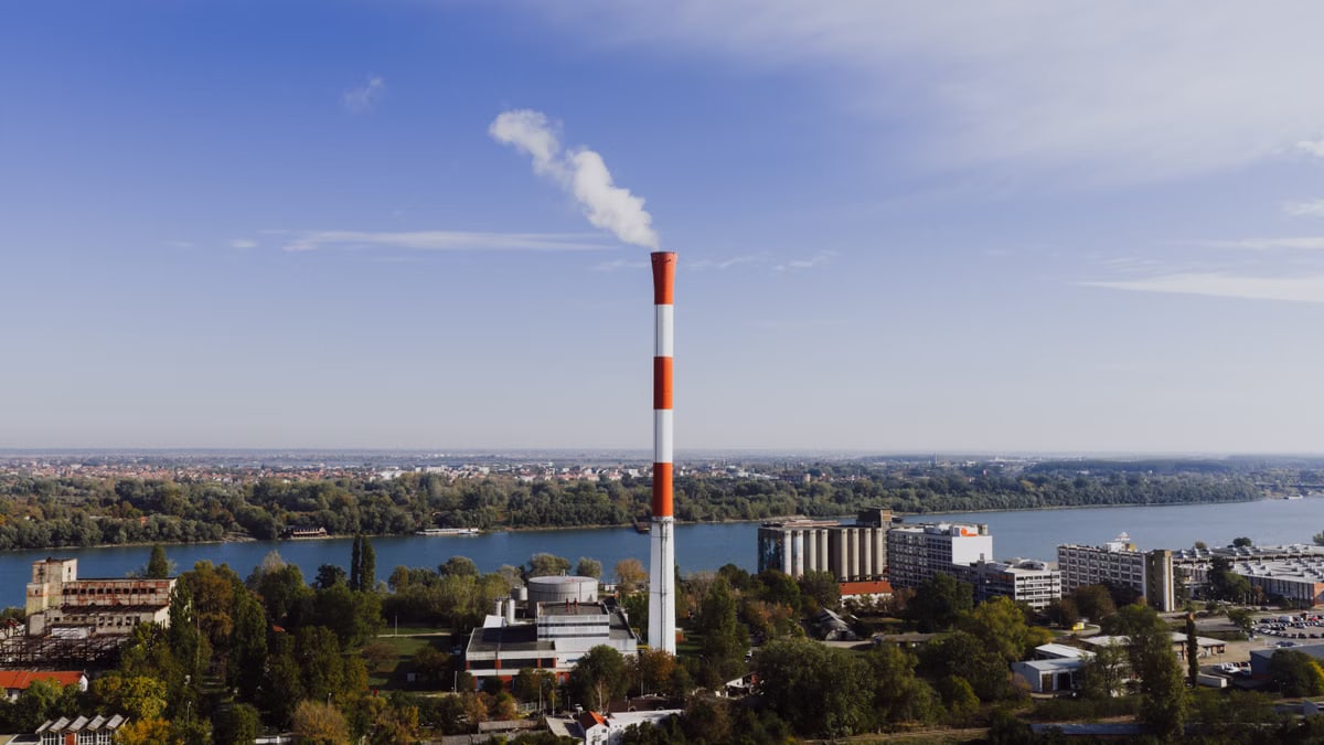 Aerial view of Belgrade's industrial area with smokestack and river on a clear day.