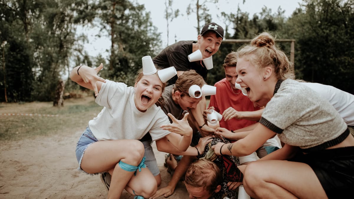 Energetic group of teenagers playing outdoors, with laughter and cups in a pile.